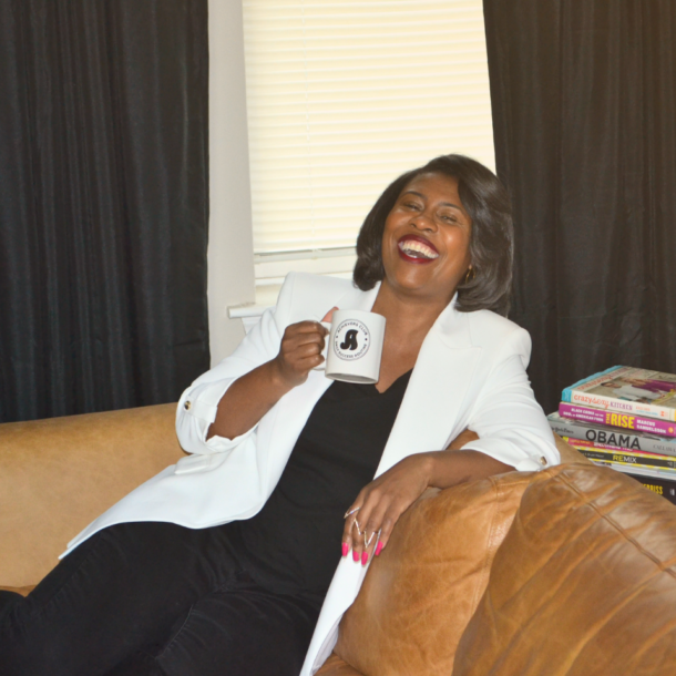 Jamila sitting on a sofa with a mug and laughing