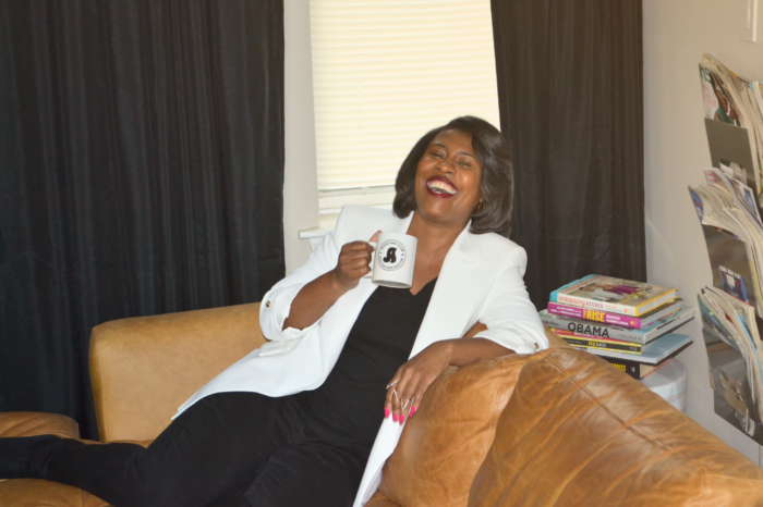 Jamila sitting on a sofa with a mug and laughing